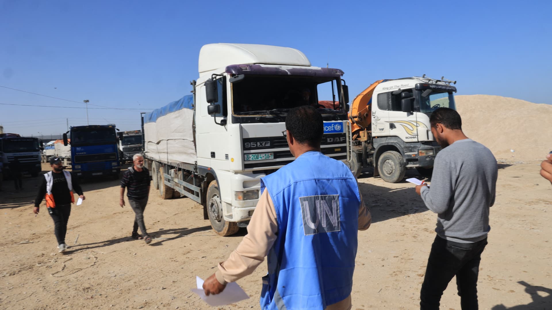 United Nations employees look on as trucks transporting humanitarian aid enter the Gaza Strip via the Rafah crossing with Egypt, hours after the start of a four-day truce in battles between Israel and Palestinian Hamas militants, on November 24, 2023. 
