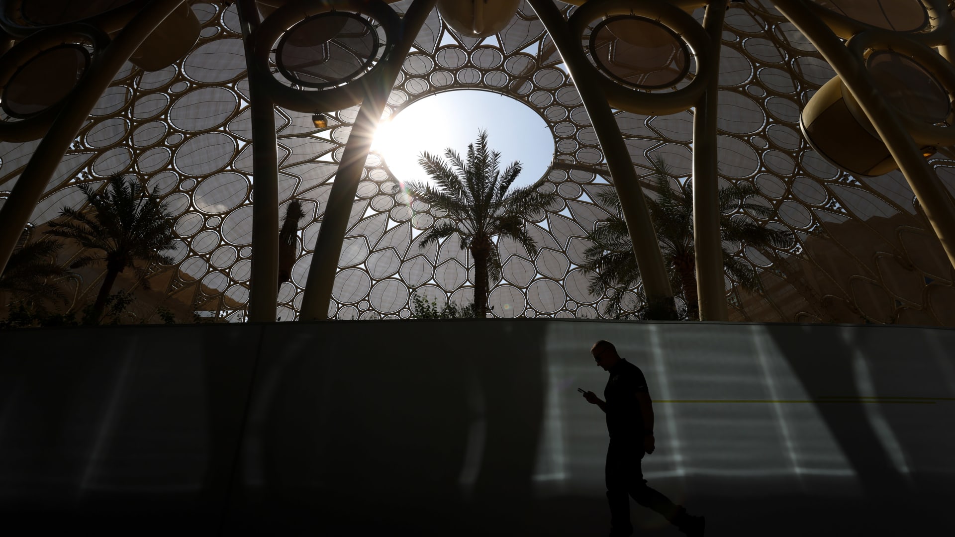 An attendee checks a smartphone whilst walking past Al Wasl dome in the Blue Zone ahead of the COP28 climate conference at Expo City in Dubai, United Arab Emirates, on Wednesday, Nov. 29, 2023. More than 70,000 politicians, diplomats, campaigners, financiers and business leaders will fly to Dubai to talk about arresting the world's slide toward environmental catastrophe.