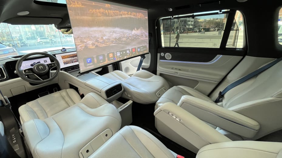 The front seats of the Aito M9 SUV can be adjusted to create reclining chairs for the second row. Passengers can watch a movie on the roll-down projector screen while storing drinks in a refrigerator compartment.