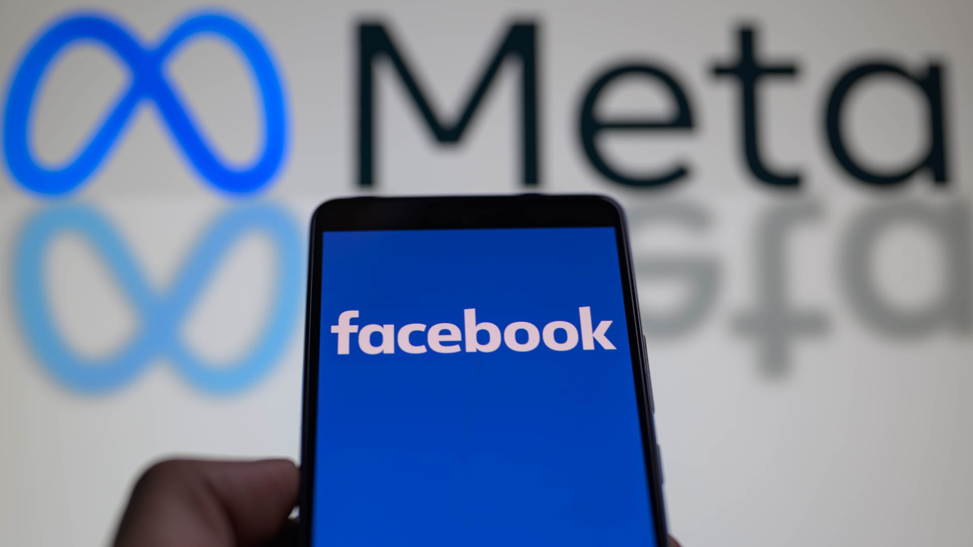 A smart phone is displaying Facebook with the Meta icon visible in the background in this photo illustration. Facebook, which was founded 20 years ago, is seen here in Brussels, Belgium, on February 4, 2024.