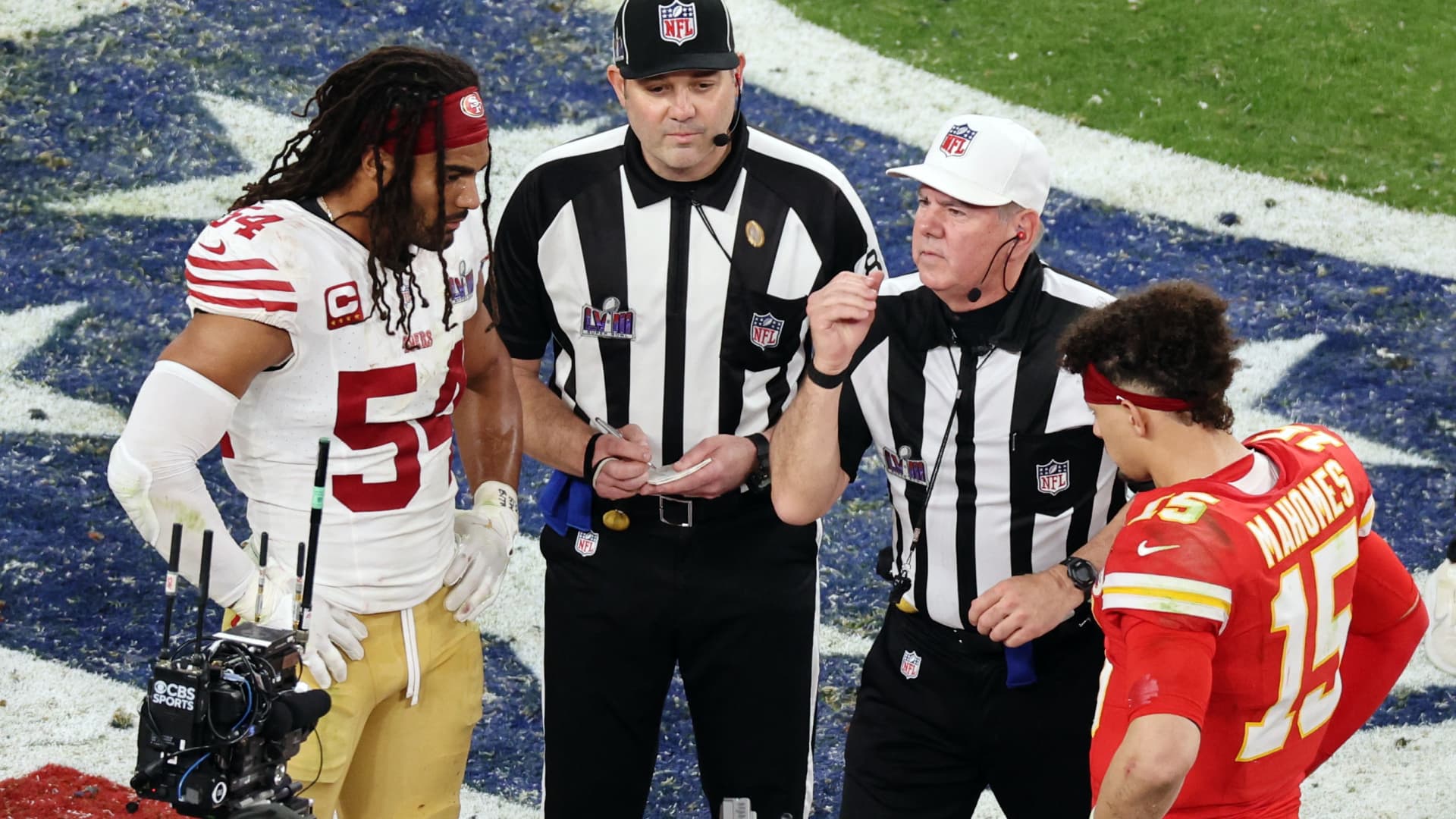 Referee Bill Vinovich performs the coin toss before overtime as San Francisco 49ers' Fred Warner and Kansas City Chiefs' Patrick Mahomes watch.