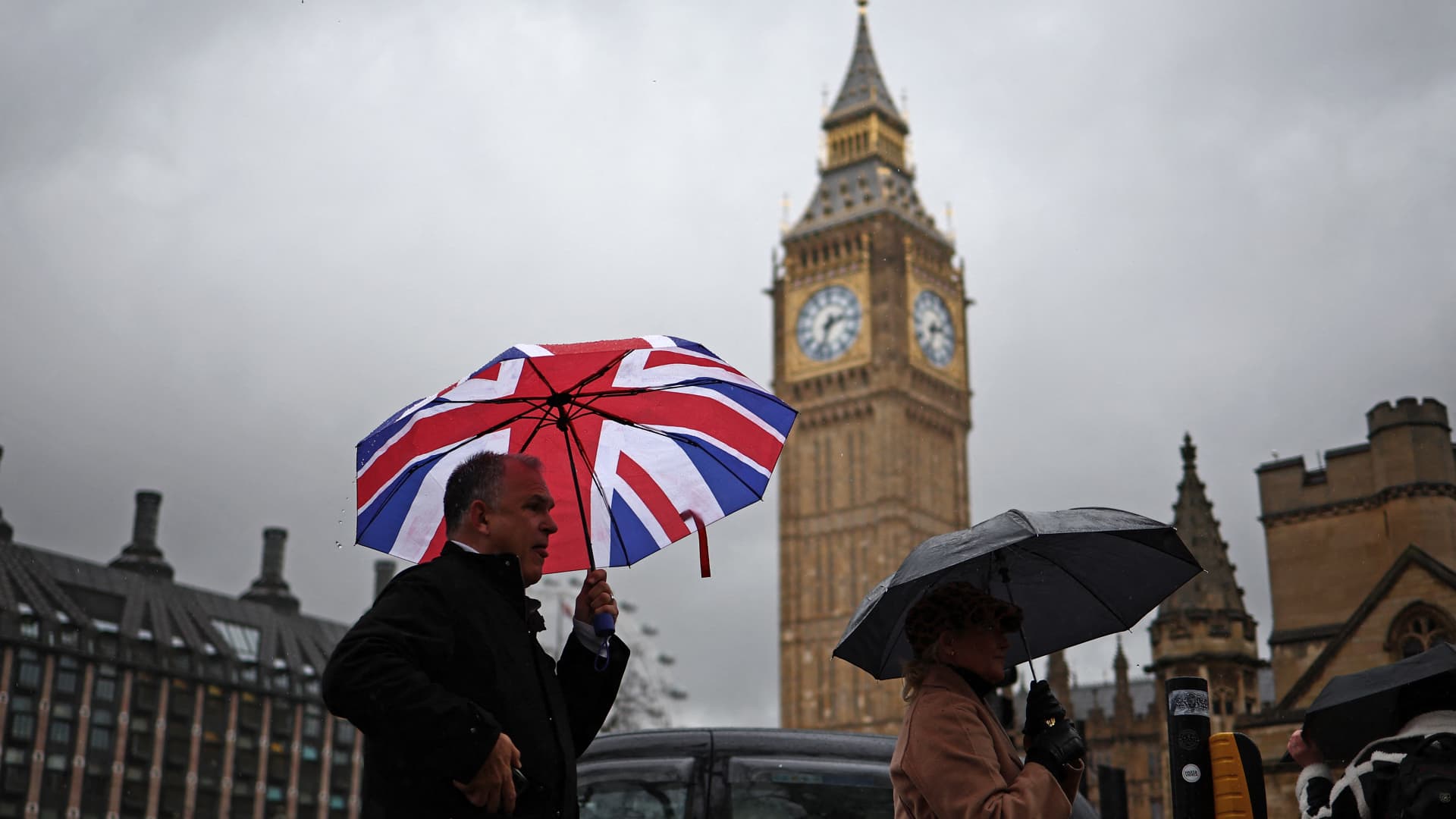 Pedestrians shelter from the rain under umbrellas as they pass the Elizabeth Tower, commonly known by the name of the clock's bell, Big Ben, at the Palace of Westminster, home to the Houses of Parliament, in London on Feb. 22, 2024.