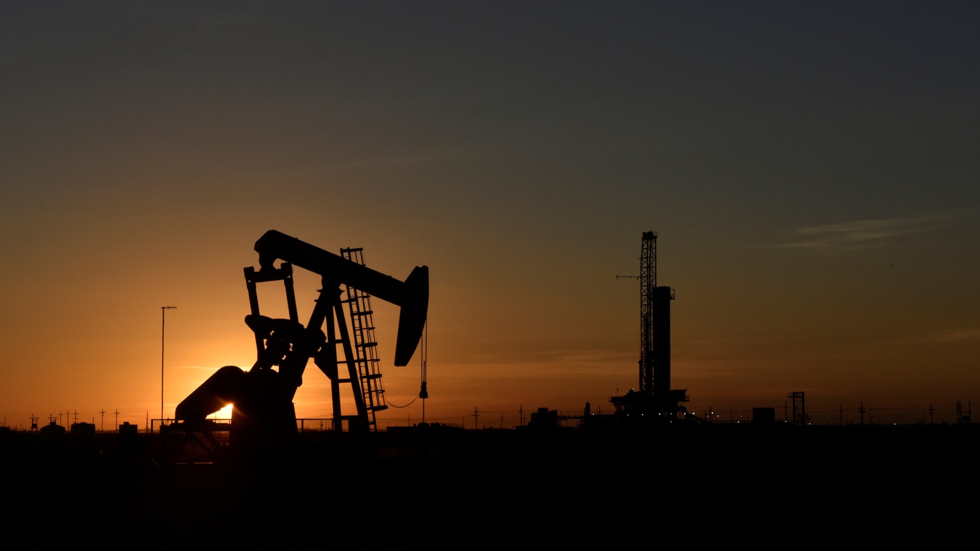 A pump jack operates in front of a drilling rig at sunset in an oil field in Midland, Texas U.S. August 22, 2018.