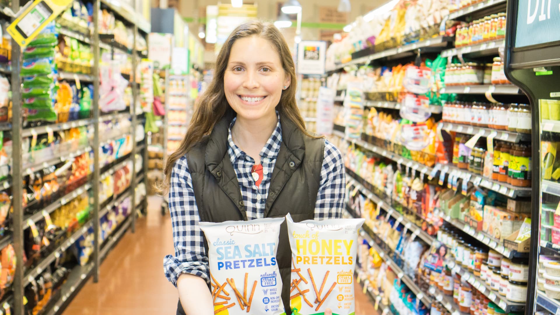 Quinn Snacks founder Kristy Lewis showing off her snacks in a grocery aisle.