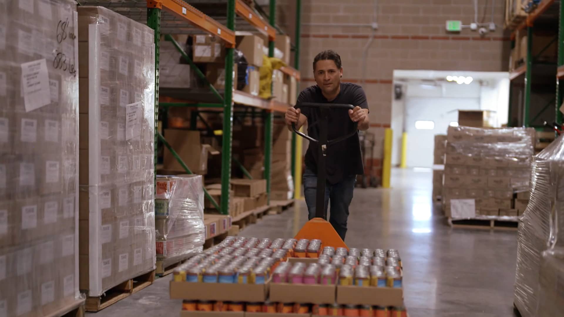 Frescos Naturales founder Juan Stewart maneuvers a cart laden with cases of his sparkling fruit drinks inside a warehouse.