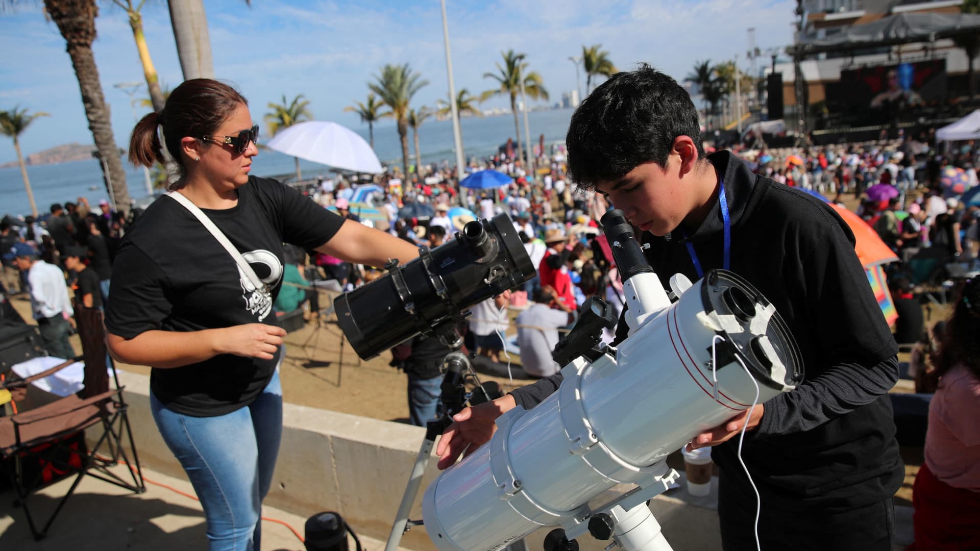 A youngster and a woman prepare their telescopes as people gather and wait to observe a total solar eclipse in Mazatlan, Mexico April 8, 2024.