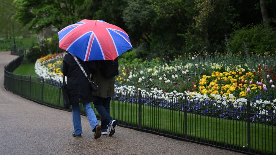 People shelters from the rain beneath a Union flag-themed umbrella as they walk past spring flowers in blossom, in St James's Park in central London on April 10, 2024. (Photo by JUSTIN TALLIS / AFP) (Photo by JUSTIN TALLIS/AFP via Getty Images)
