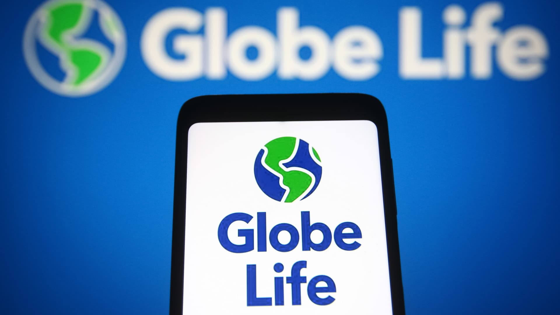 In this photo illustration, Globe Life logo is seen on a smartphone and pc screen. 