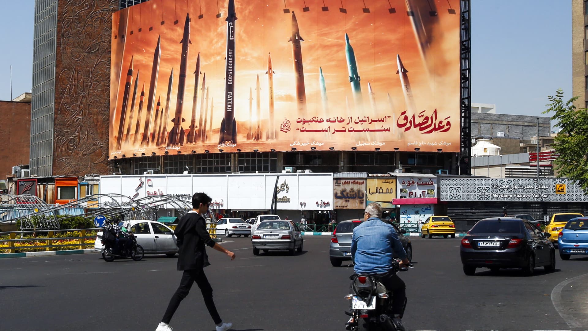 A man crosses a street as motorists drive past a billboard depicting Iranian ballistic missiles in service in Tehran on April 19, 2024.