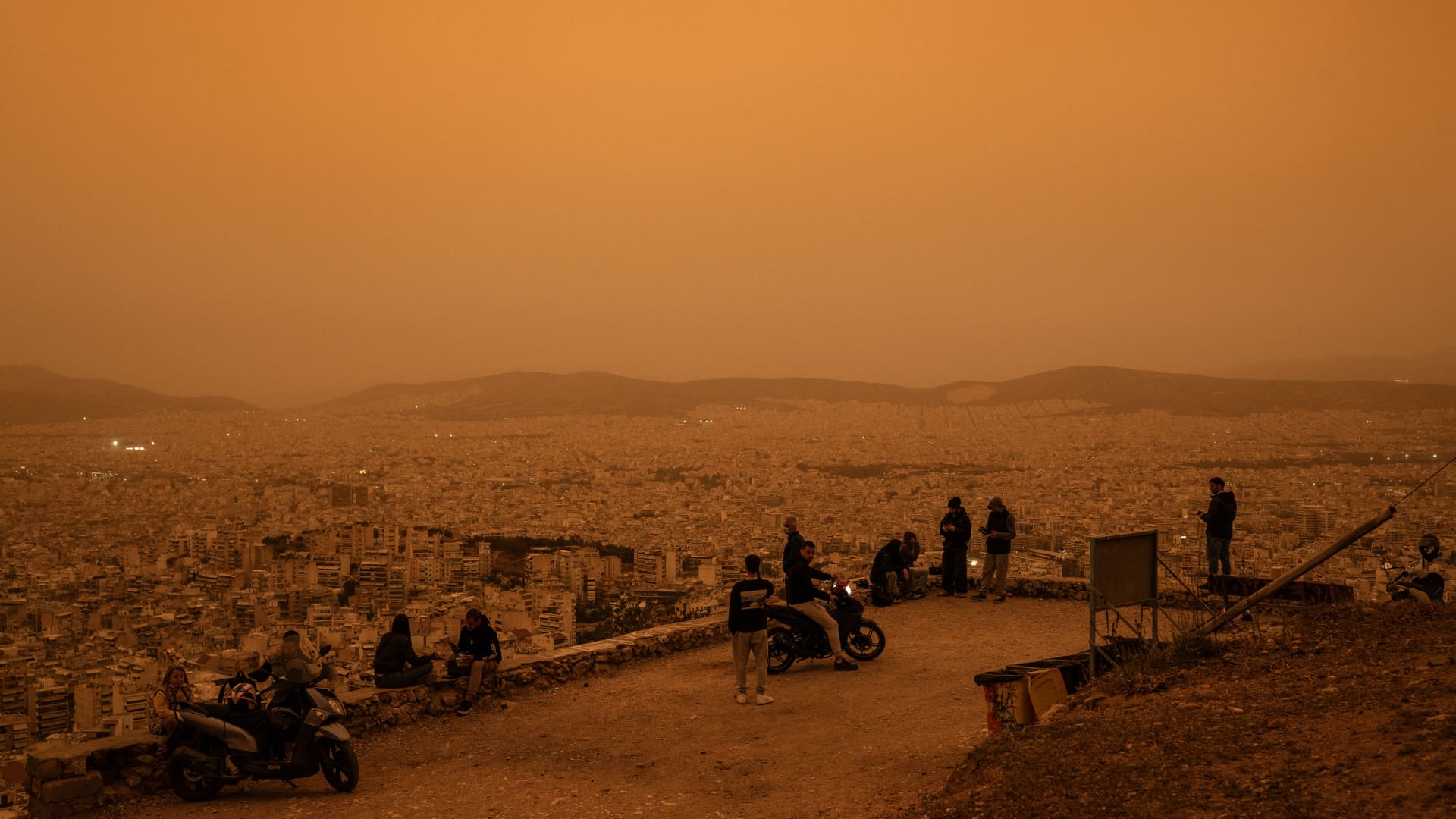 People sit on Tourkovounia hill overlooking the city of Athens, as southerly winds carry waves of Saharan dust to the city, in Athens, on April 23, 2024.